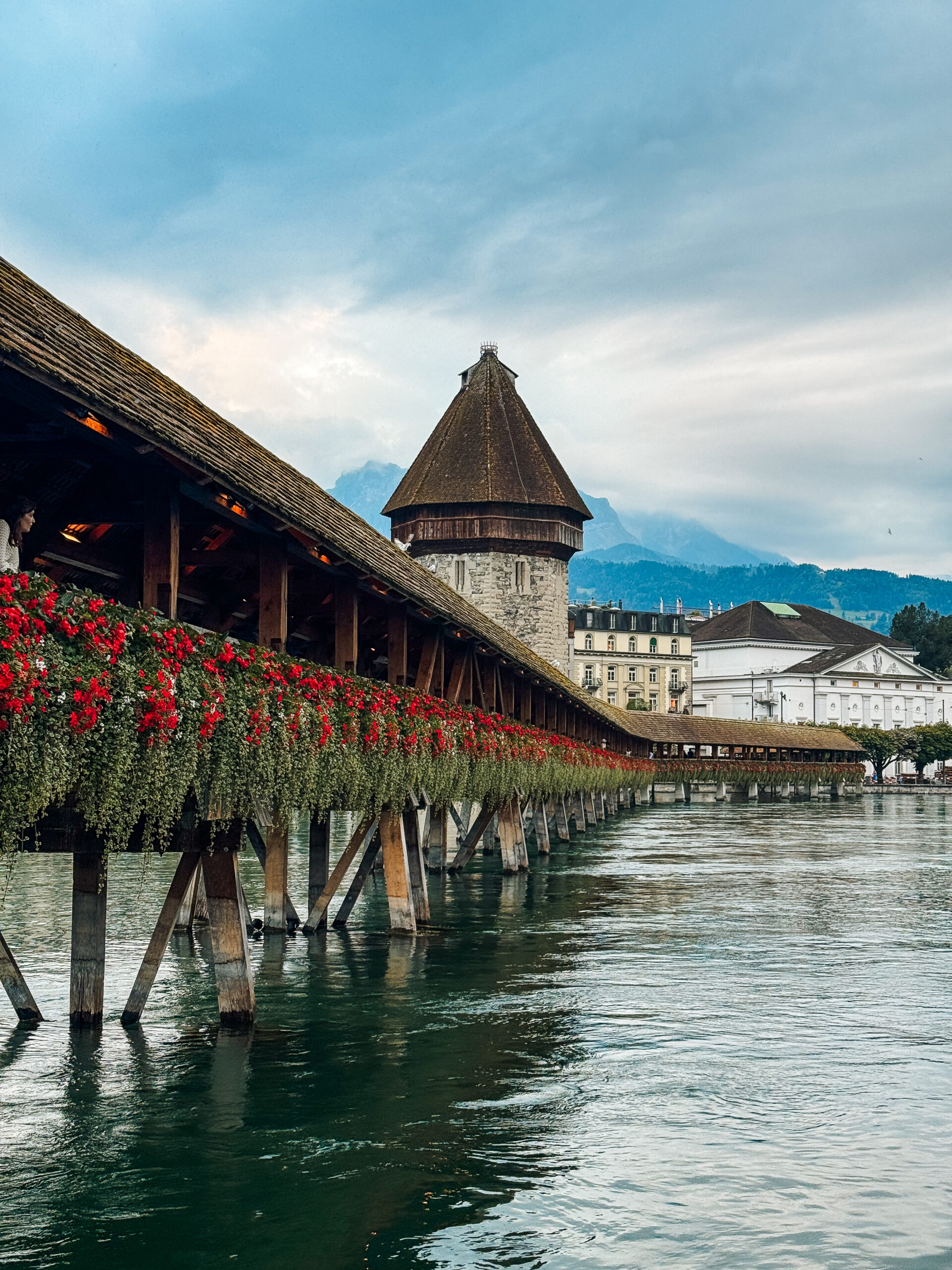Covered wooden bridge lined with vibrant red flowers, leading toward the Water Tower.