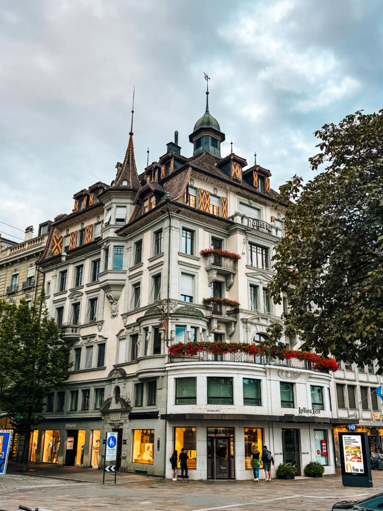 Elegant old building with turrets, flower-decked balconies, and shops on the ground floor.