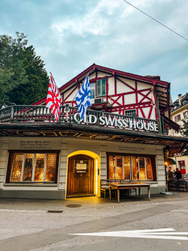 Traditional Swiss restaurant with timber-framed exterior, bright window lights, and flags above the entrance.