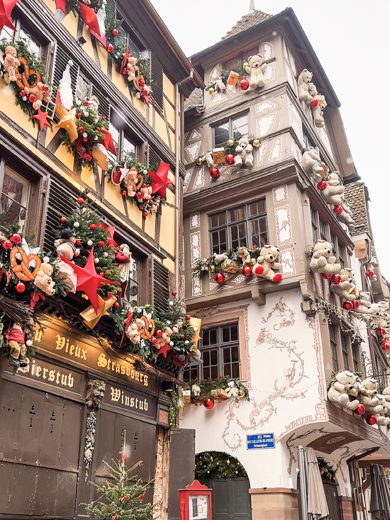 Half timbered building in Strasbourg decorated with giant teddy bears, red ornaments, and festive garlands during Christmas.