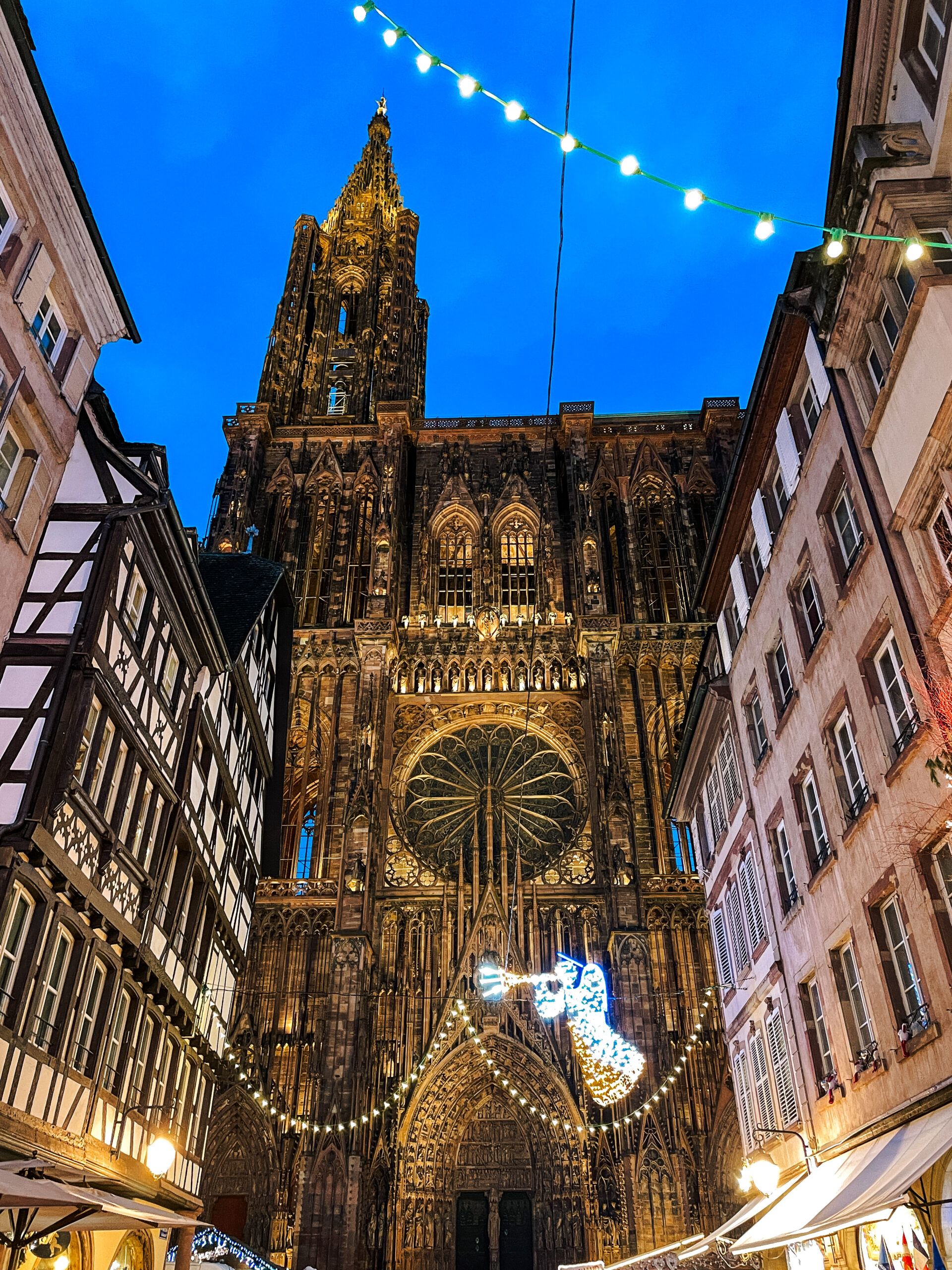 Strasbourg Cathedral towering above half timbered houses at dusk with festive Christmas lights and angel decoration.