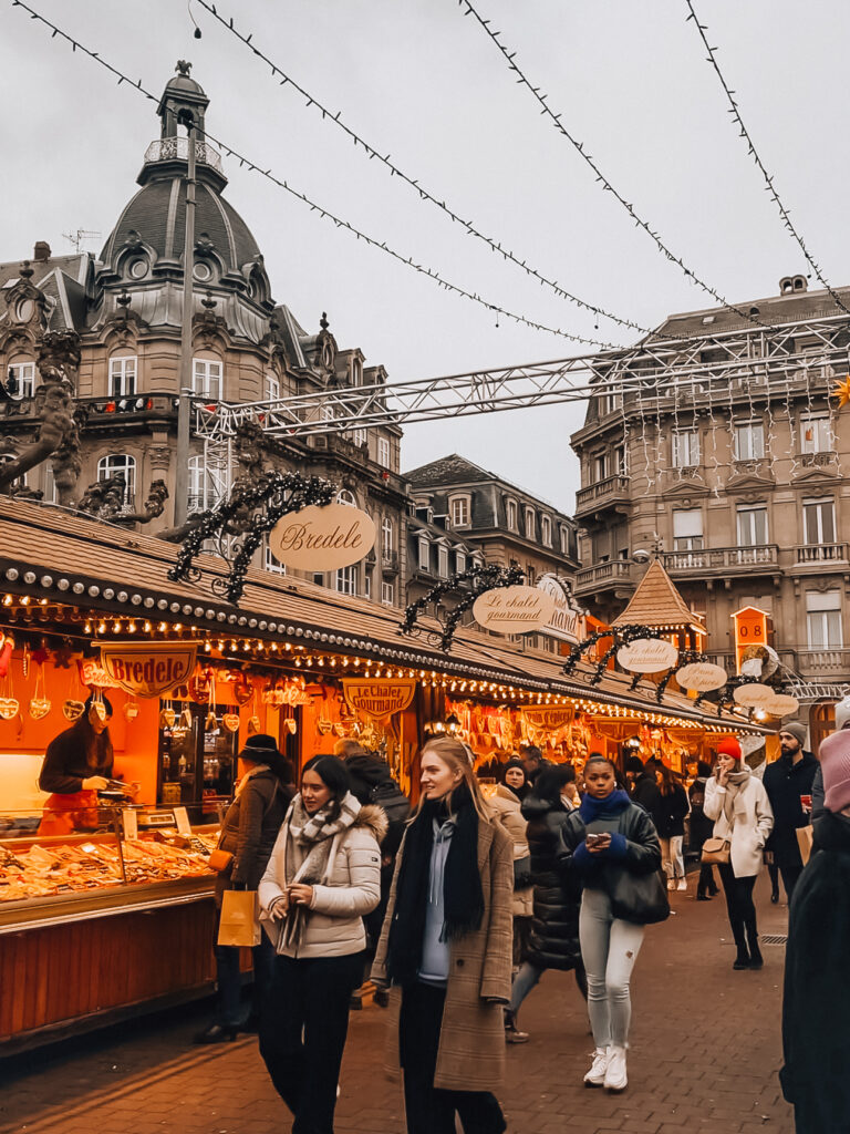 Crowds shopping at wooden chalets selling Bredele cookies and festive treats at Strasbourg Christmas market in Place Broglie