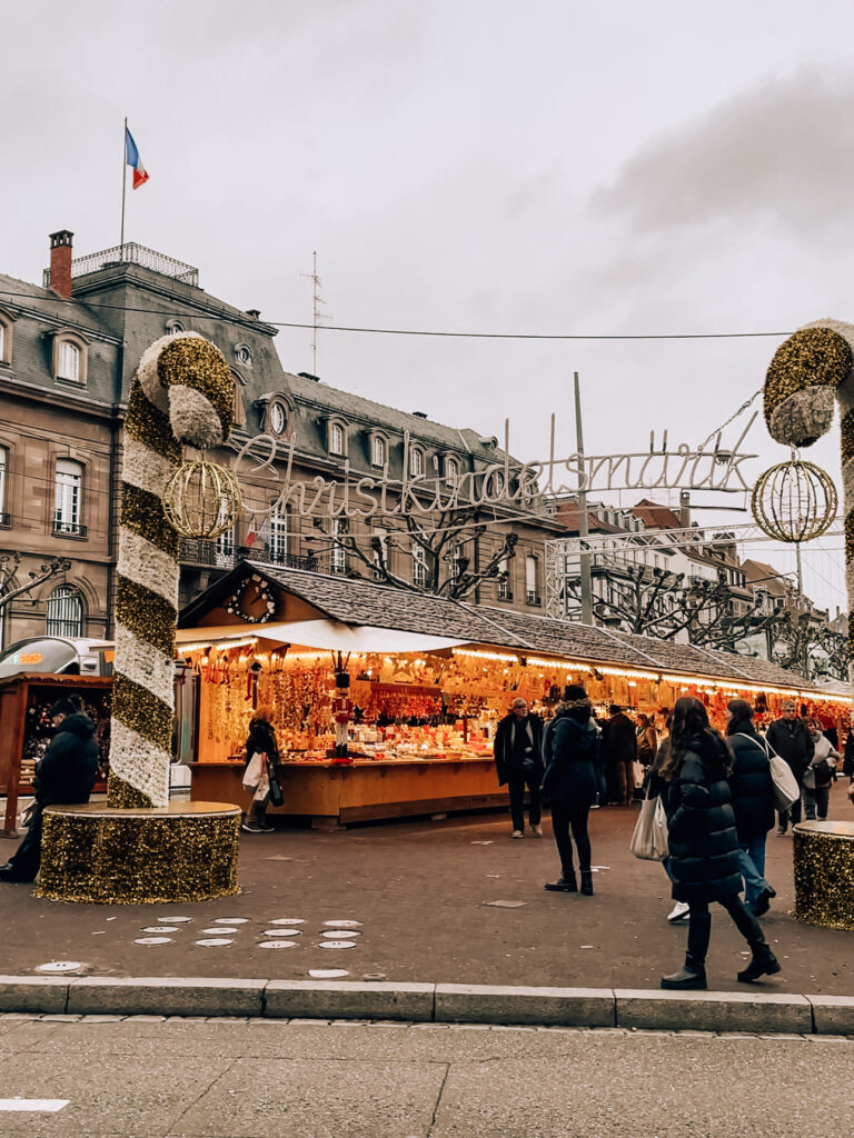 Entrance to Strasbourg’s Christkindelsmärik with candy cane decorations and stalls selling Christmas gifts.