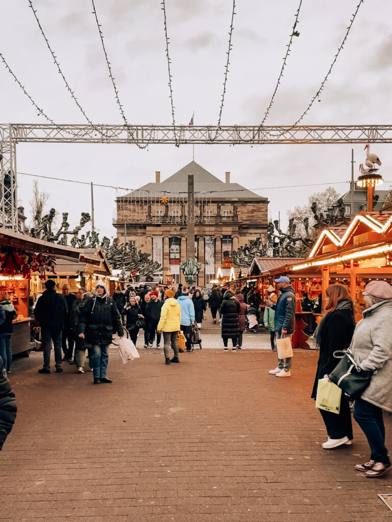 Crowds walking among wooden chalets selling festive gifts and treats at Strasbourg Christmas market in Place Broglie