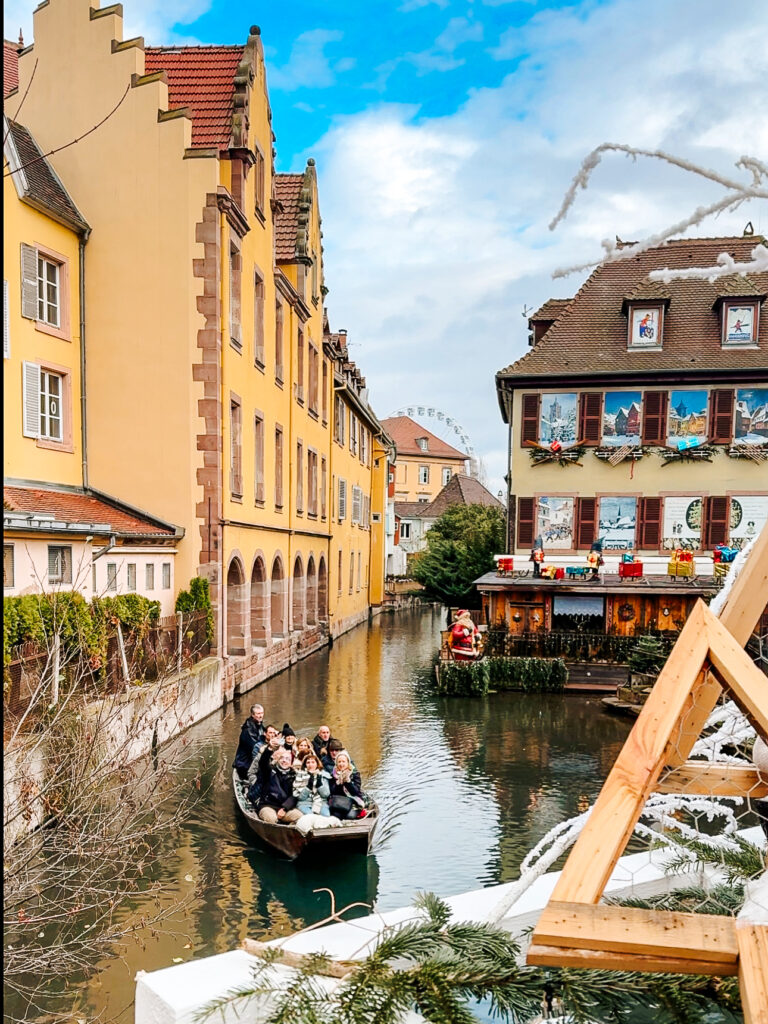 Tourists enjoying a boat ride through canals lined with colorful Alsatian houses in Colmar at Christmas.