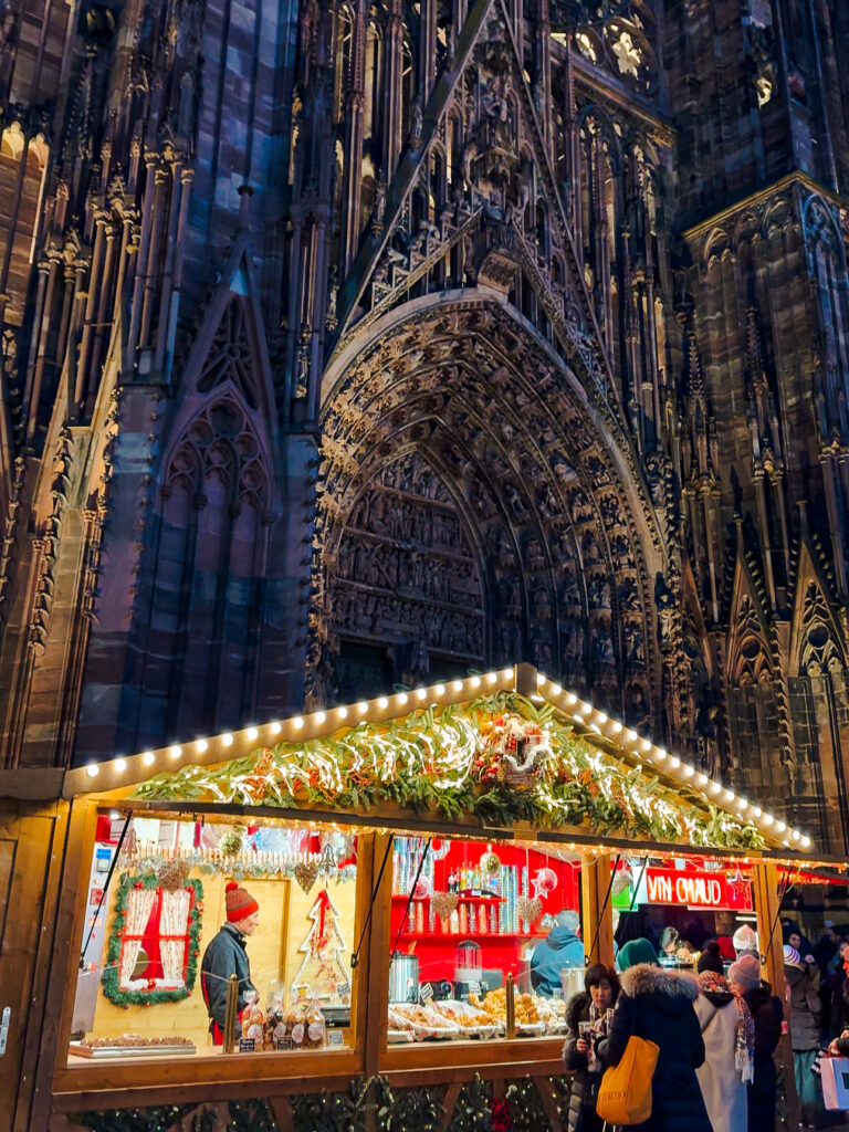 Wooden Christmas market stall selling gingerbread and hot drinks in front of Strasbourg Cathedral.