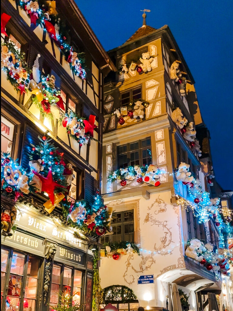 Famous Strasbourg teddy bear house lit up at night with Christmas lights, oversized teddy bears, and ornaments on the façade.