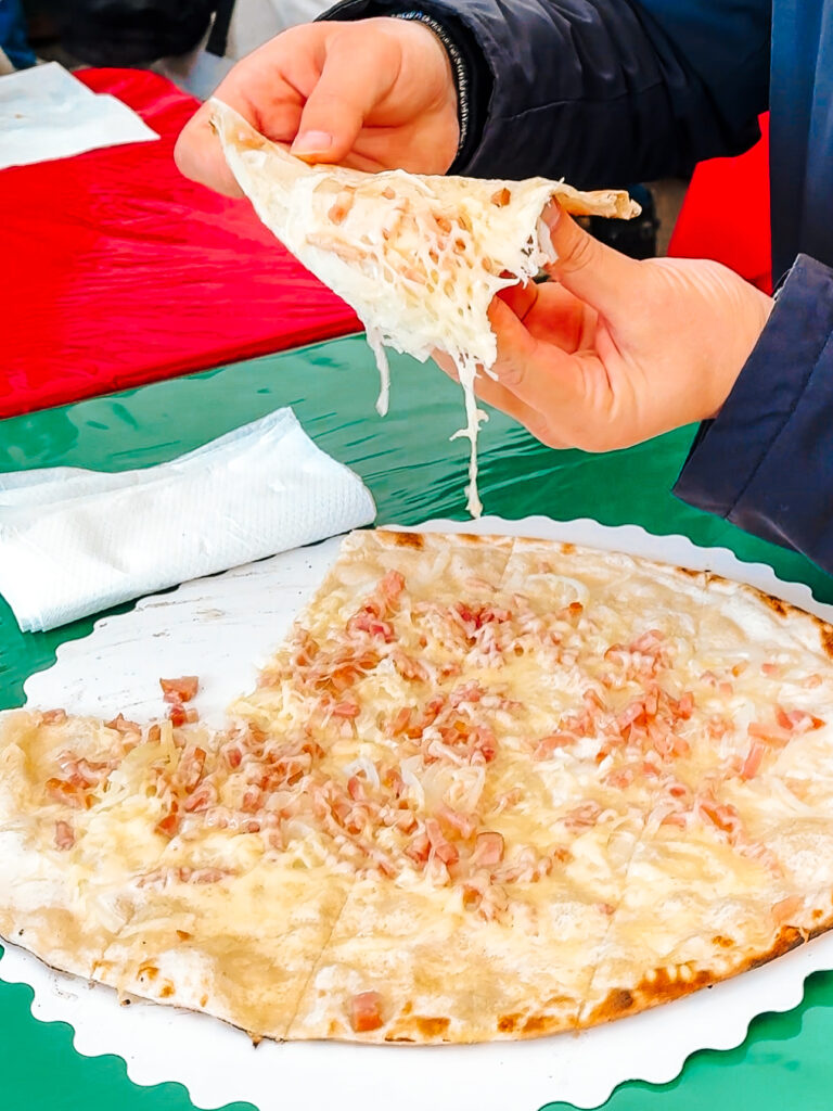 Traditional Alsatian tarte flambée with onions, cream, and bacon being served hot at Strasbourg Christmas market.