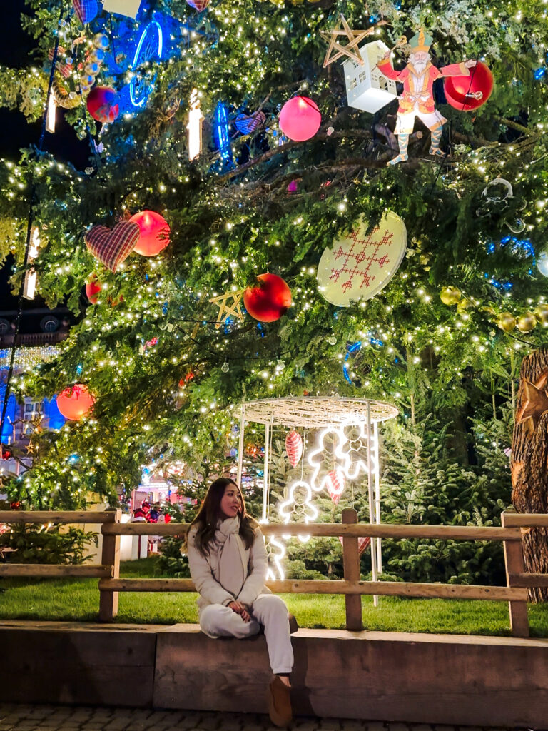 Traveler sitting beneath the illuminated Grand Sapin Christmas tree at Place Kléber in Strasbourg.