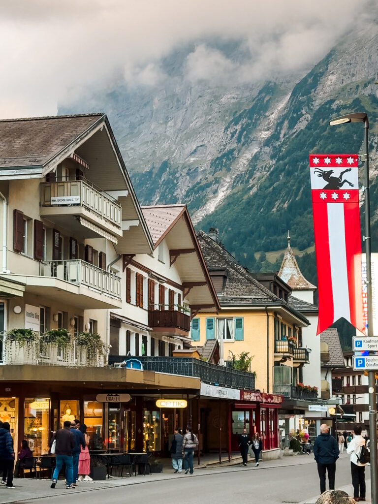 Central Grindelwald village scene with shops, Swiss flags, and traditional alpine buildings surrounded by steep mountain cliffs