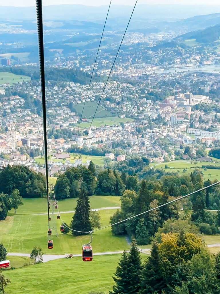 Red gondola cabins moving up the cable line with sweeping views over Lucerne and the green valley below.