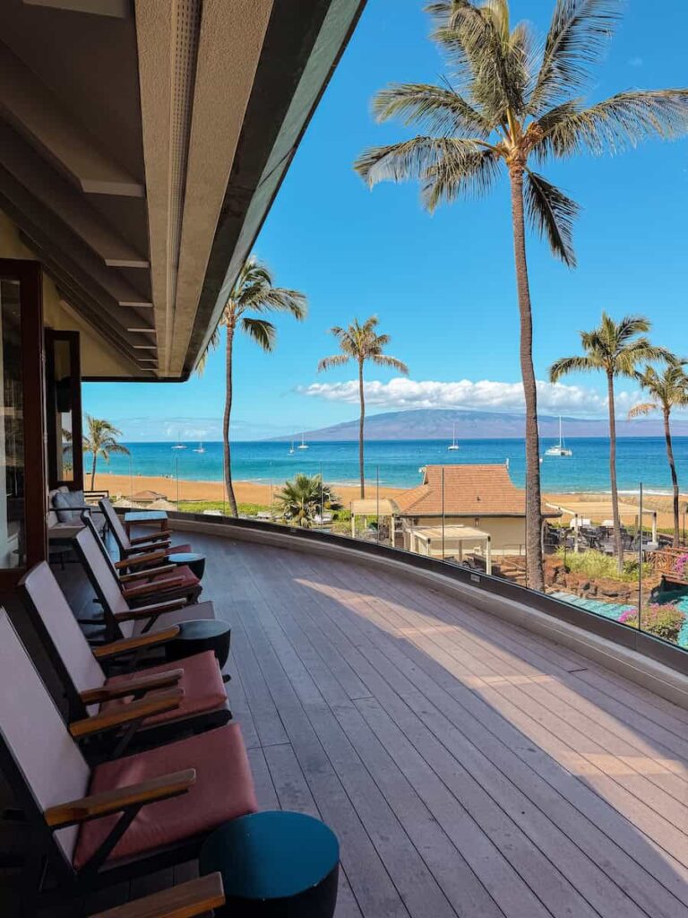 Oceanfront terrace lined with lounge chairs overlooking Kaʻanapali Beach and the island of Lānaʻi in the distance at Sheraton Maui Resort.
