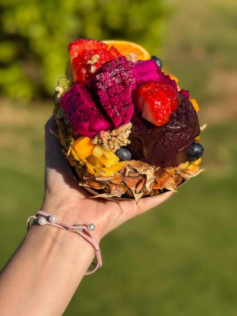 Vibrant pineapple acai bowl from Maui Ninja Fruit filled with dragon fruit, strawberries, mango, and blueberries held under the Hawaiian sun