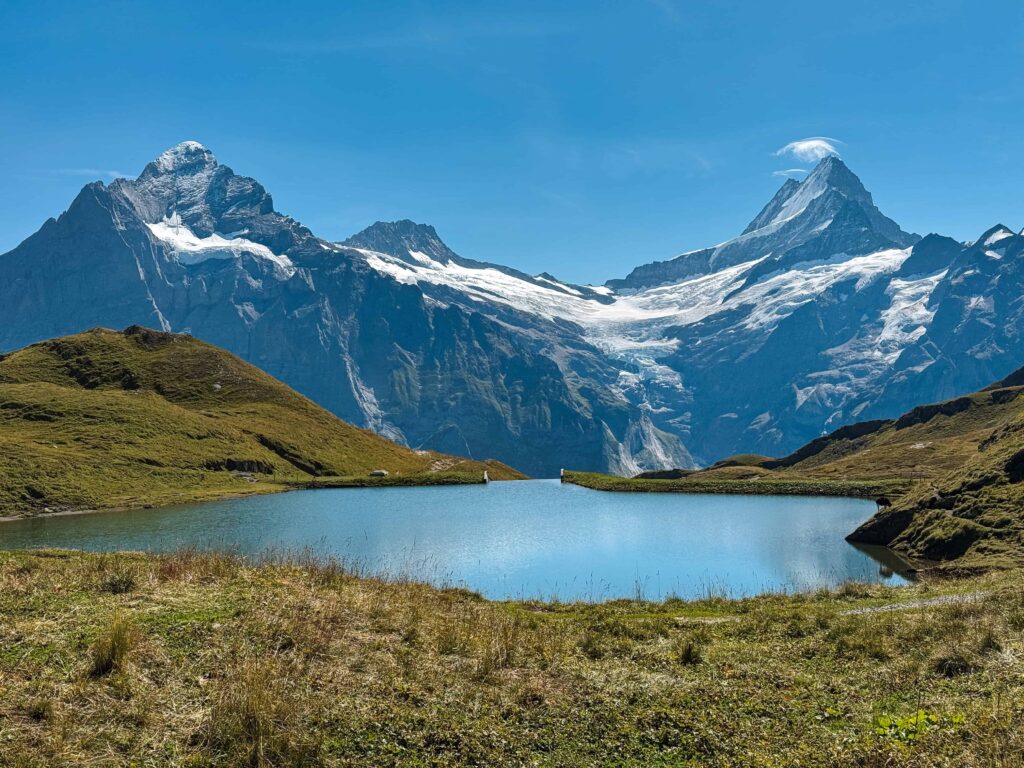 Traditional wooden Swiss chalet adorned with red flower boxes sits in front of dramatic rocky mountain cliffs partially covered in clouds in Gimmelwald, Switzerland which is a must visit in a Switzerland Itinerary