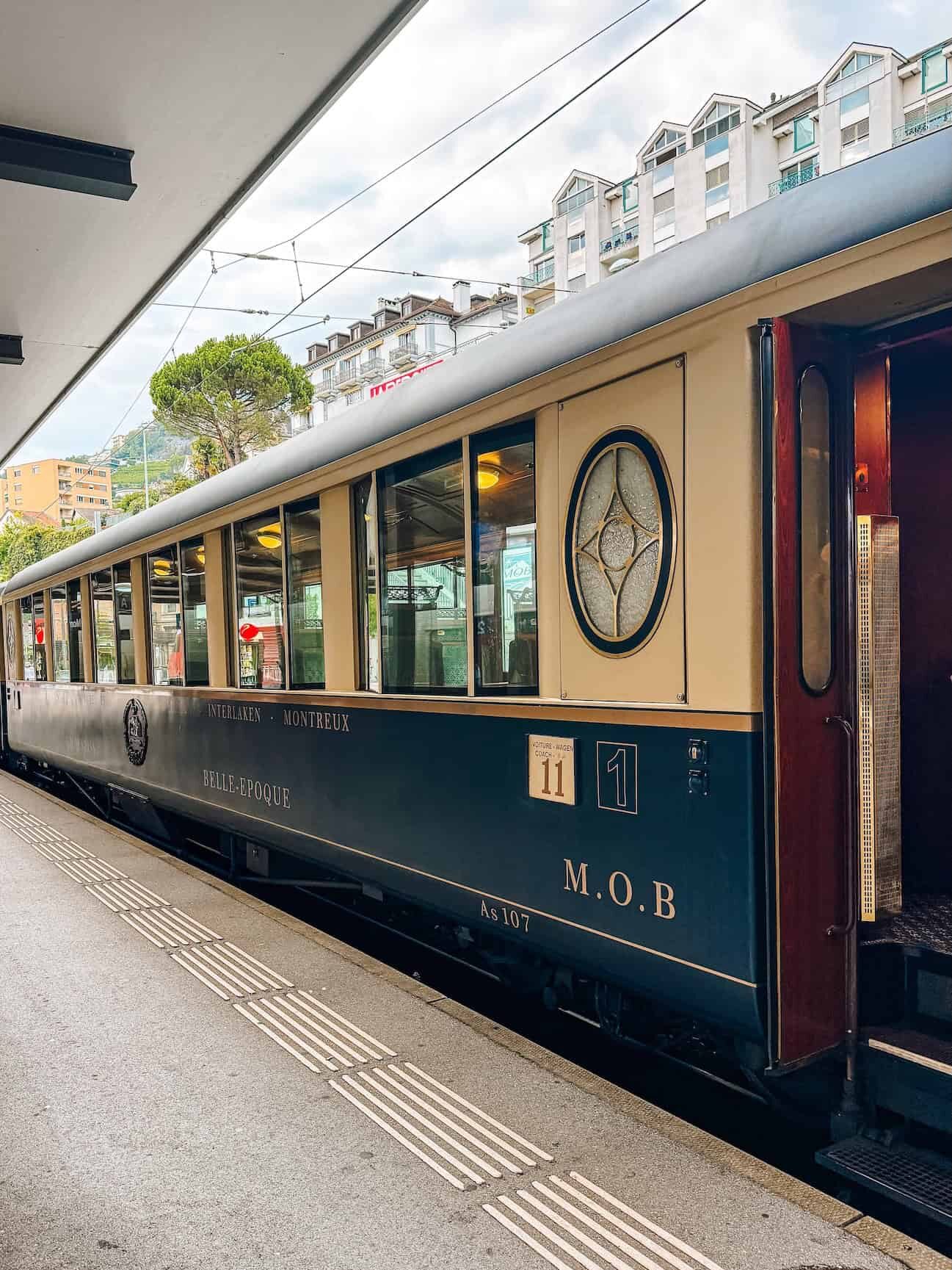 The GoldenPass Belle Epoque train at the station in Montreux, Switzerland, featuring its elegant cream and navy blue exterior with vintage gold lettering and art deco details, evoking the charm of early 20th-century luxury travel.