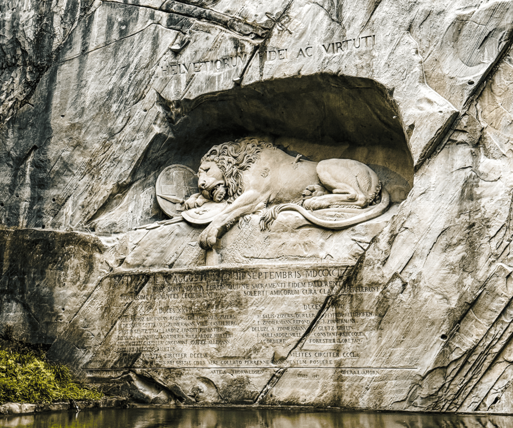 The Lion Monument in Lucerne, Switzerland, showing a detailed stone sculpture of a dying lion carved into a rock face, commemorating Swiss Guards who died during the French Revolution.