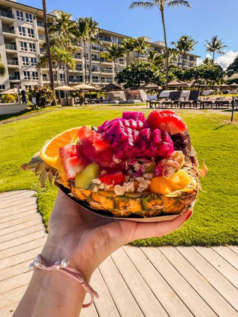 Colorful pineapple acai bowl topped with fresh tropical fruits at Maui Ninja Fruit, held in front of a beachfront resort in Kaʻanapali, Maui.