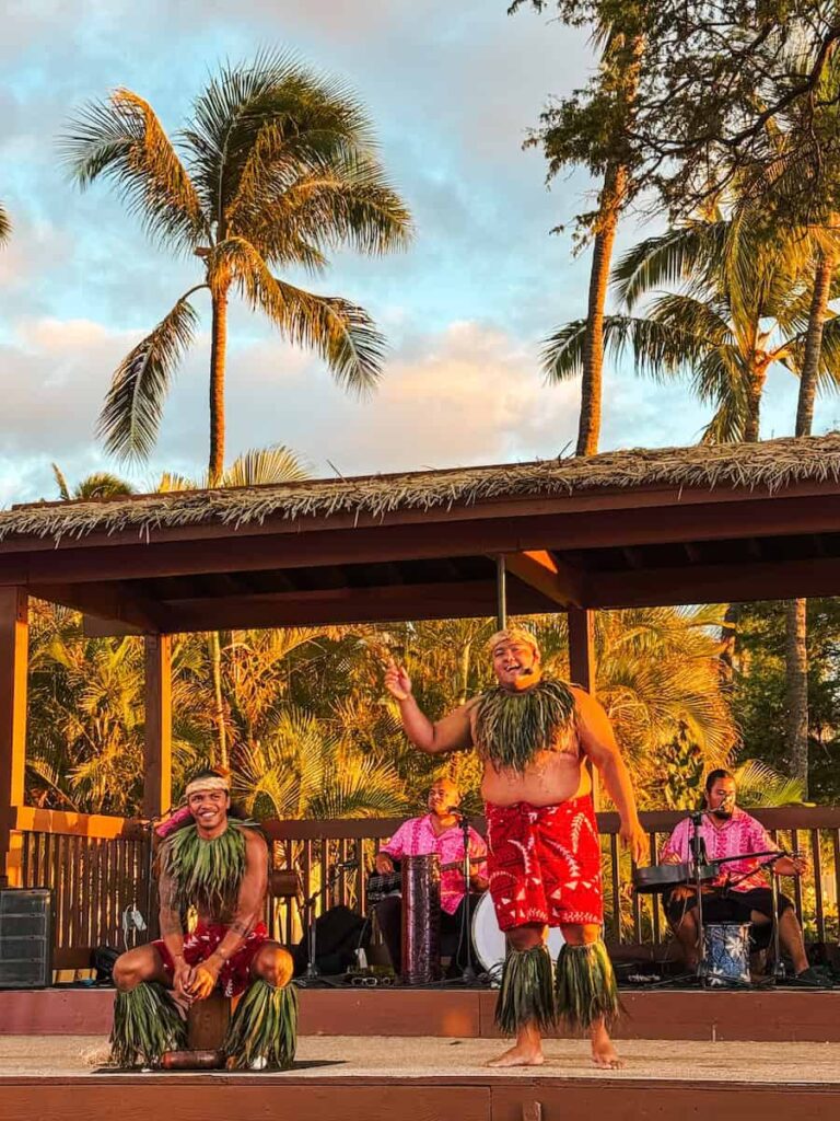 Hawaiian dancers performing at Maui Nui Luau in Lahaina with palm trees and musicians in the background during sunset 