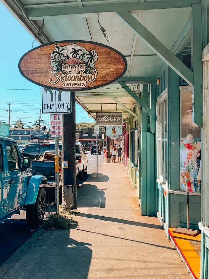 Charming small-town street in Paia, Maui, lined with boutiques and surf shops, including Moonbow Tropics under the wooden awning.