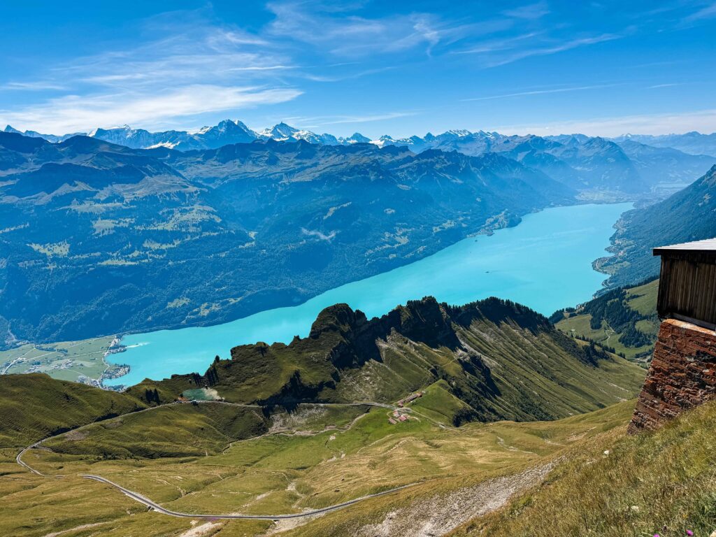 Panoramic view from Brienz Rothorn Kulm overlooking the turquoise waters of Lake Brienz surrounded by rugged alpine peaks and lush green valleys under a clear blue sky.