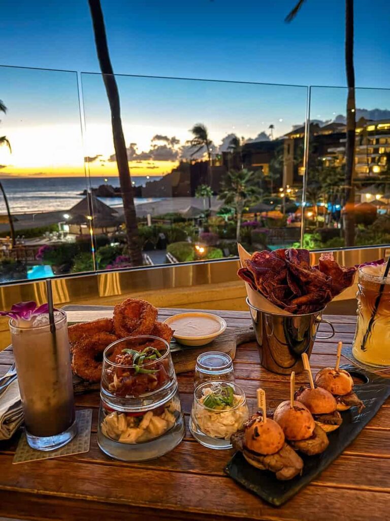 Dinner spread with cocktails, poke, and sliders at The Sandbar in Sheraton Maui Resort, overlooking Kaʻanapali Beach during sunset.