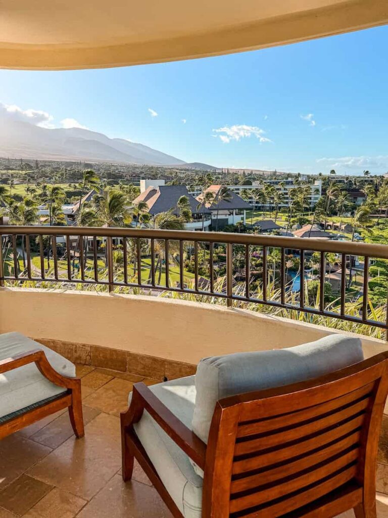 Two wooden lounge chairs on a private balcony at Sheraton Maui Resort overlooking palm trees, golf greens, and mountains in the distance