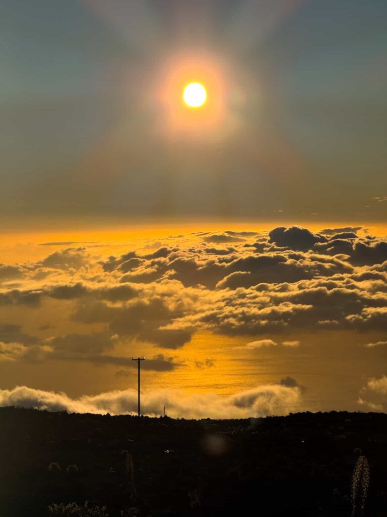 The sun shining over glowing clouds during sunset at Haleakalā National Park, casting golden light across the sky and ocean.
