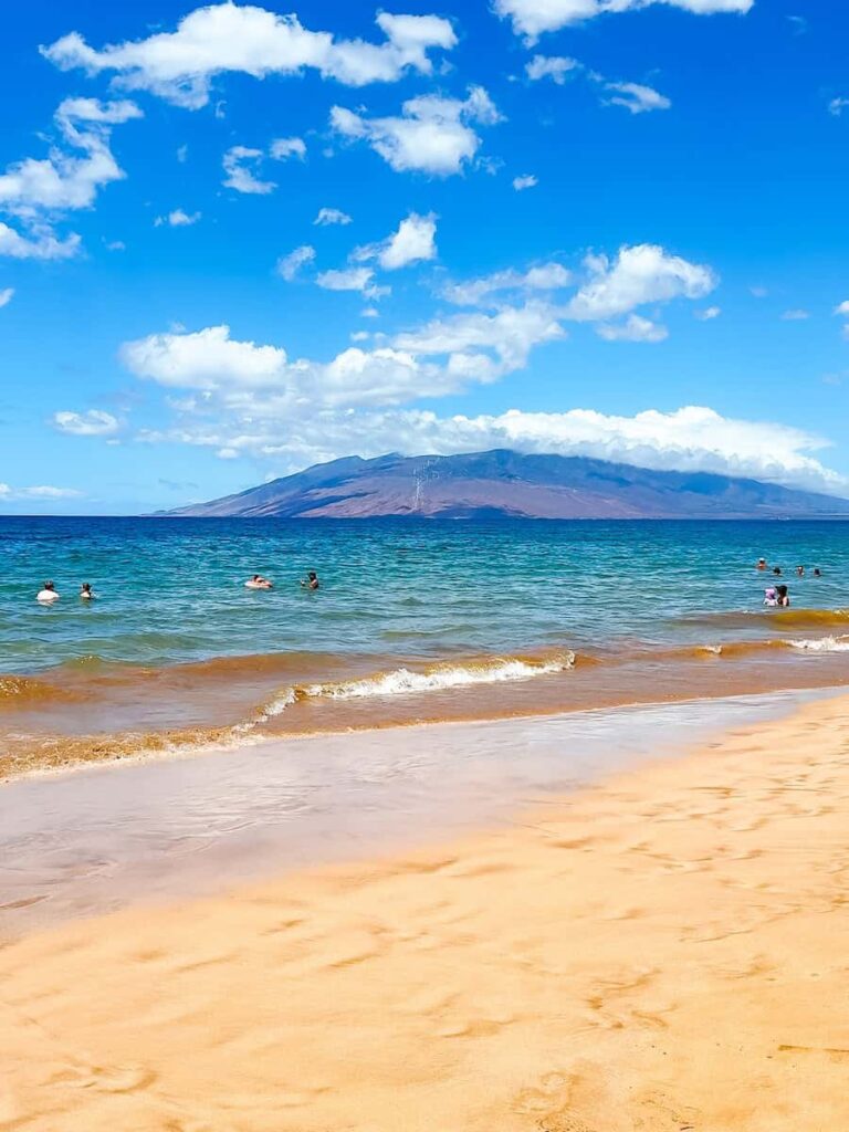 Golden sand and calm blue waves at Wailea Beach in Maui with views of the nearby island of Kahoʻolawe under a bright blue sky.