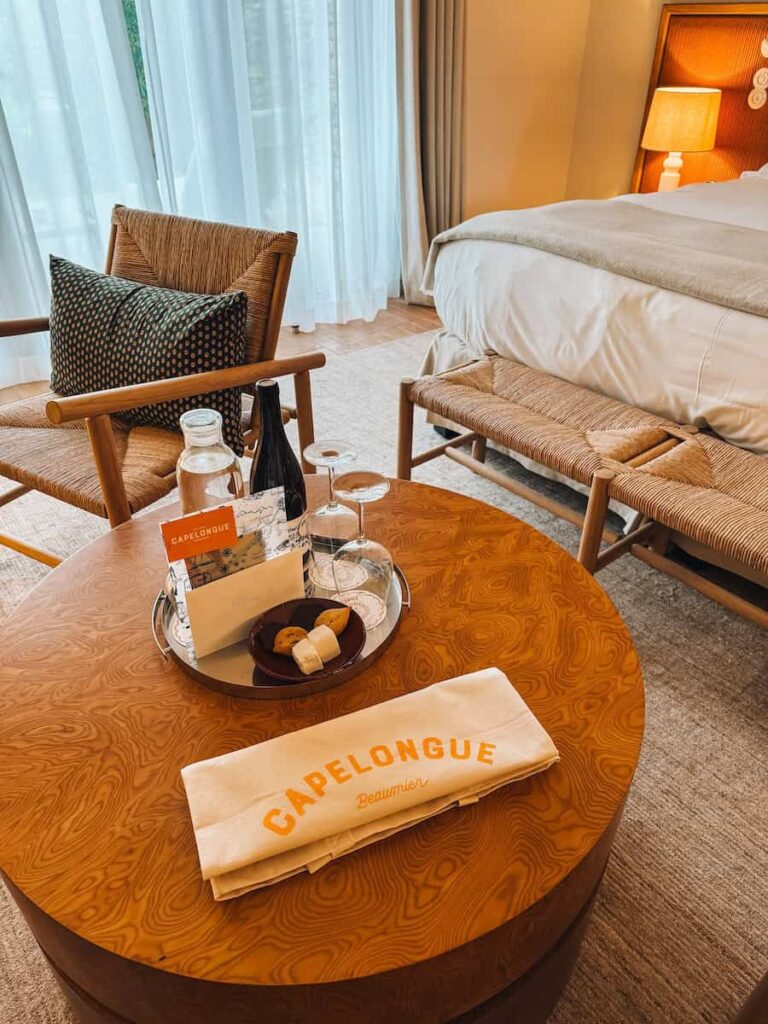 A welcome tray with wine, glasses, and small pastries placed on a round wooden table in a softly lit room.