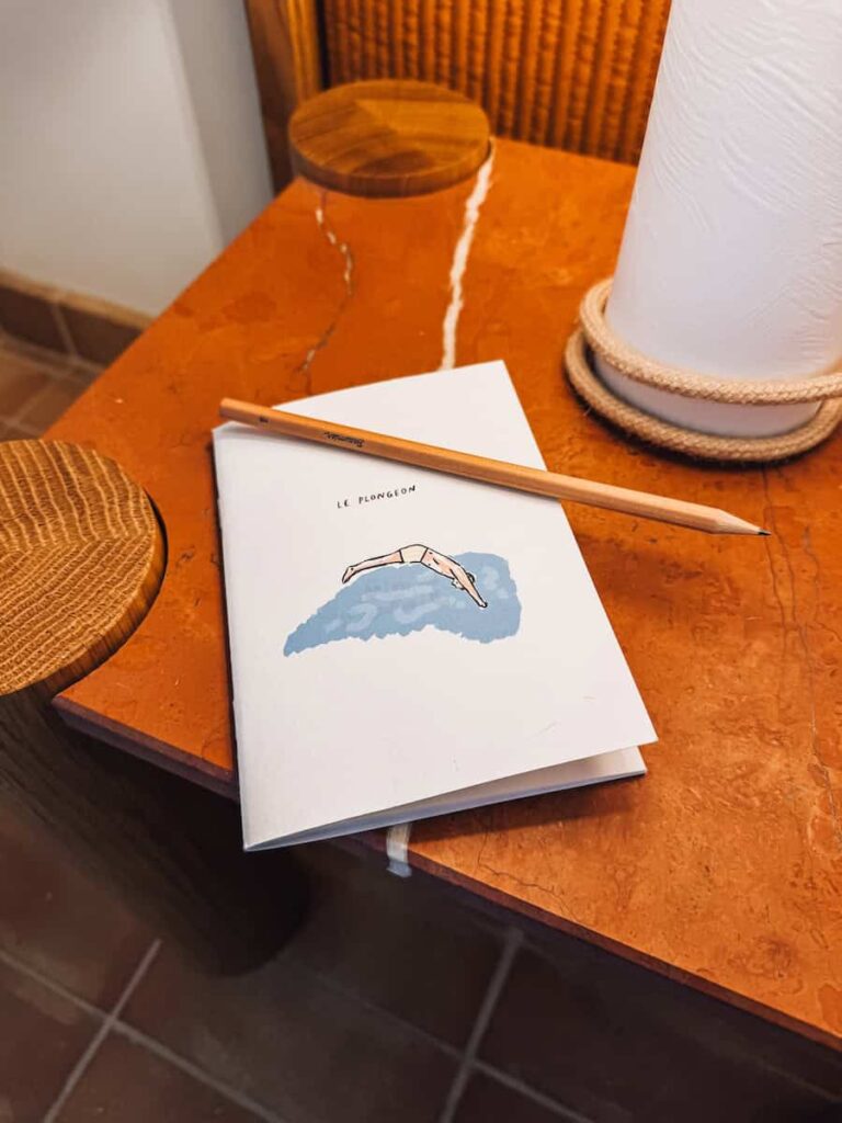 A small illustrated notebook and wooden pencil resting on a bedside table with a terracotta surface.