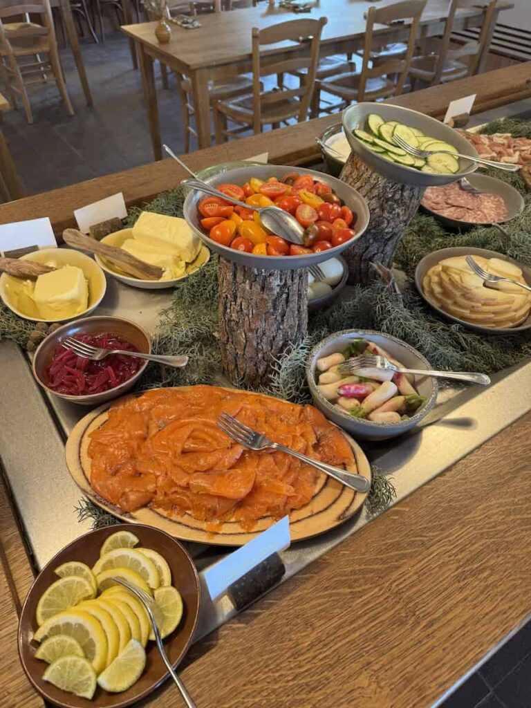A breakfast buffet display featuring smoked salmon, fresh vegetables, cheeses, and pickled sides.