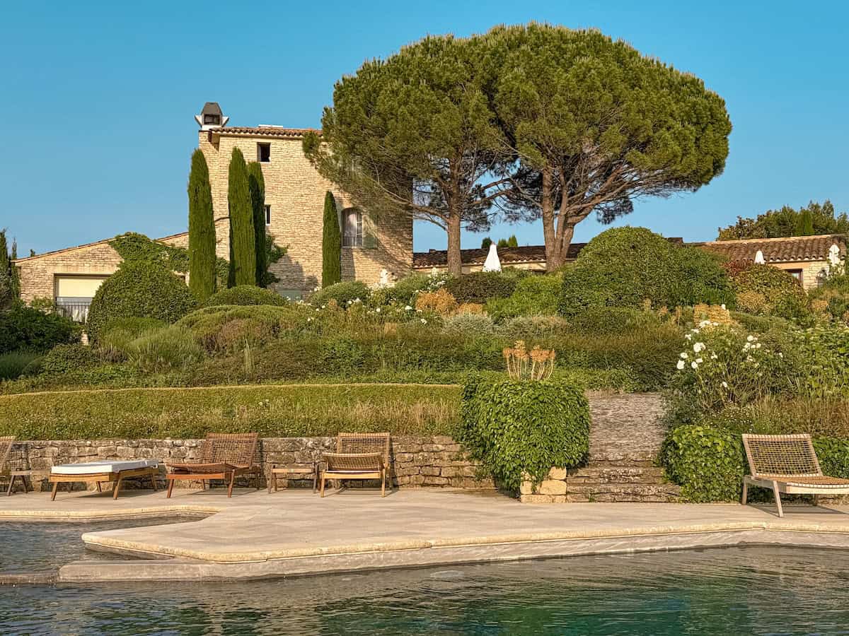 A hillside view of a rustic stone estate with cypress trees and gardens above a pool terrace at Capelongue hotel in Provence