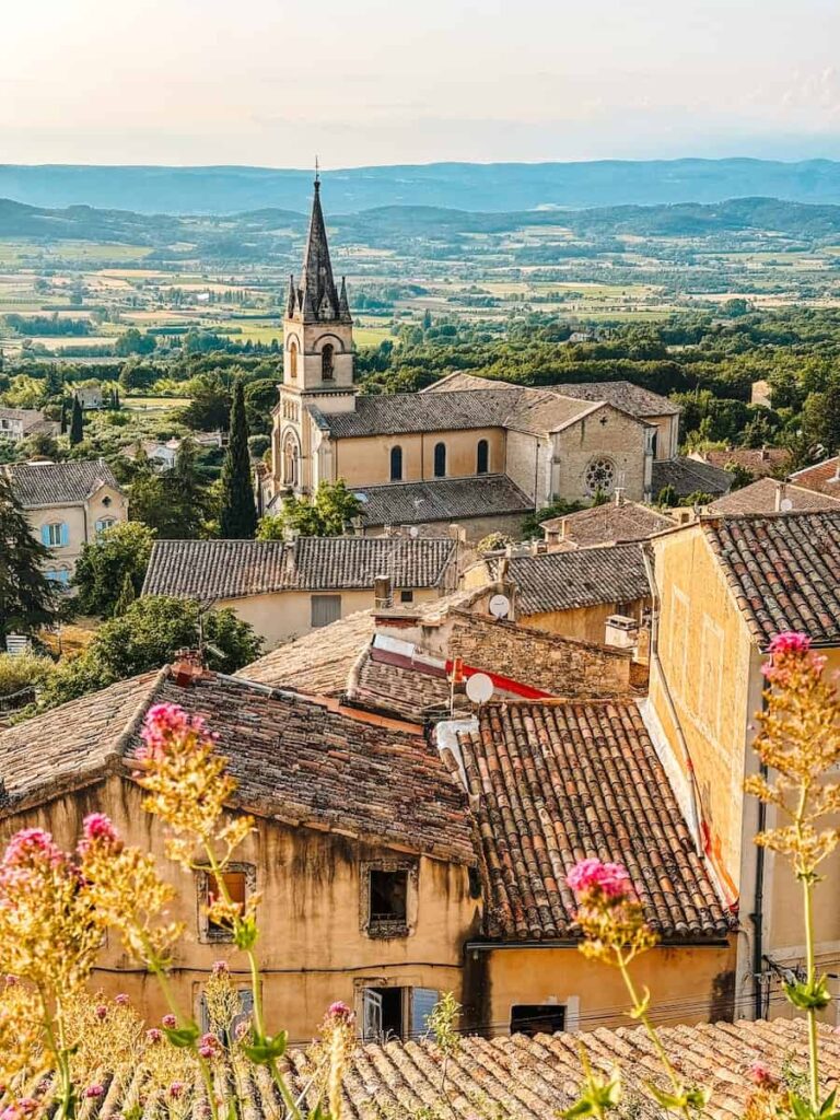 A panoramic view of a hilltop village with a church spire and terracotta rooftops overlooking the valley.
