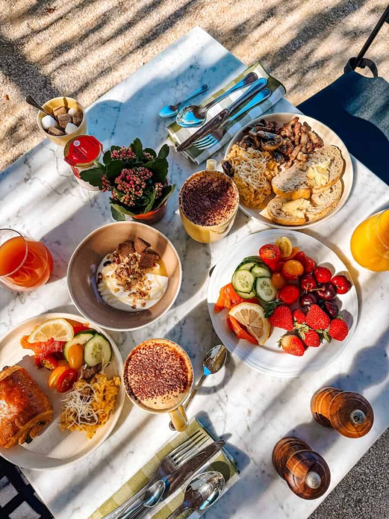 A table setting with breakfast plates of fruit, croissants, meats, coffee, and juice.