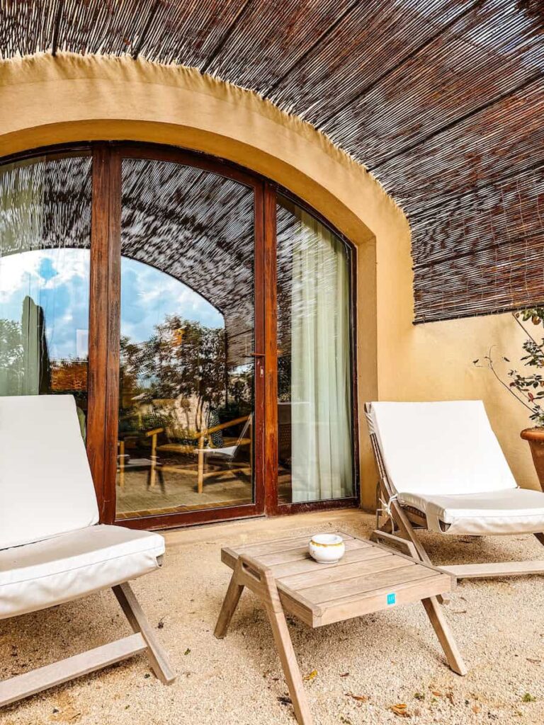A private outdoor terrace with cushioned lounge chairs and a small wooden table under a woven shade canopy.