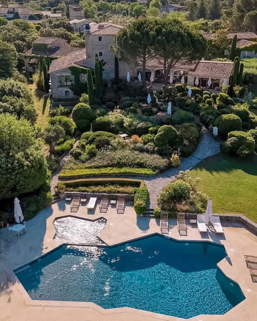 Aerial view of Capelongue’s terraced gardens and swimming pool surrounded by stone buildings and cypress trees.