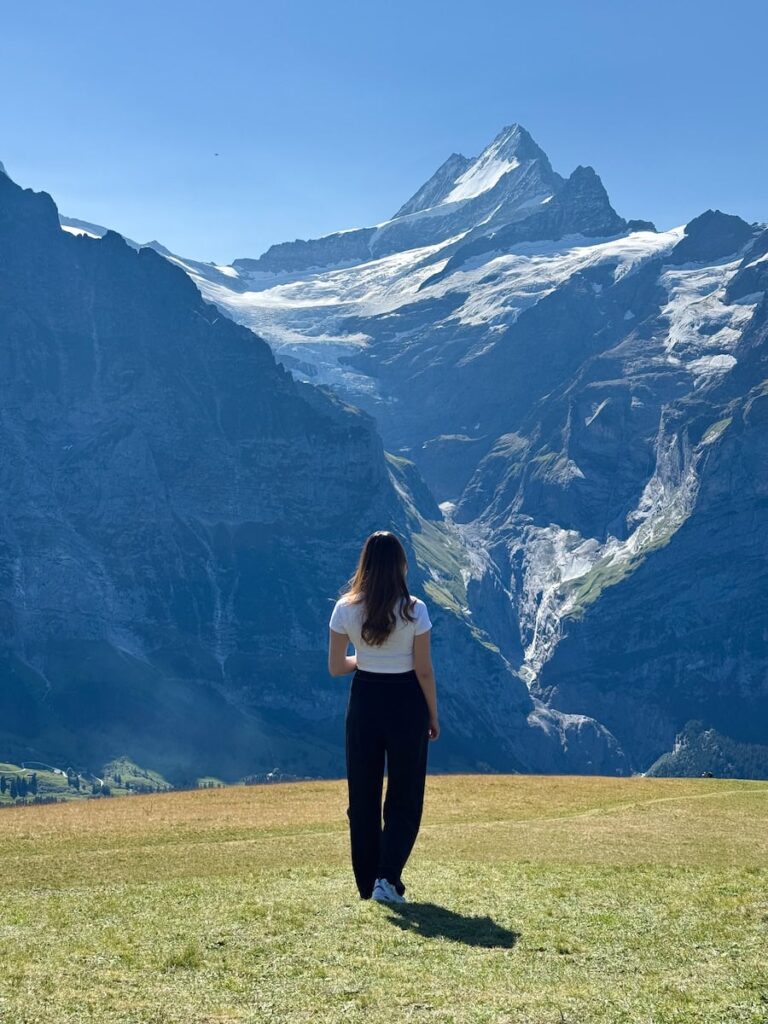 Woman standing in an open meadow at Grindelwald First while looking toward the towering glacier covered peaks of the Swiss Alps.