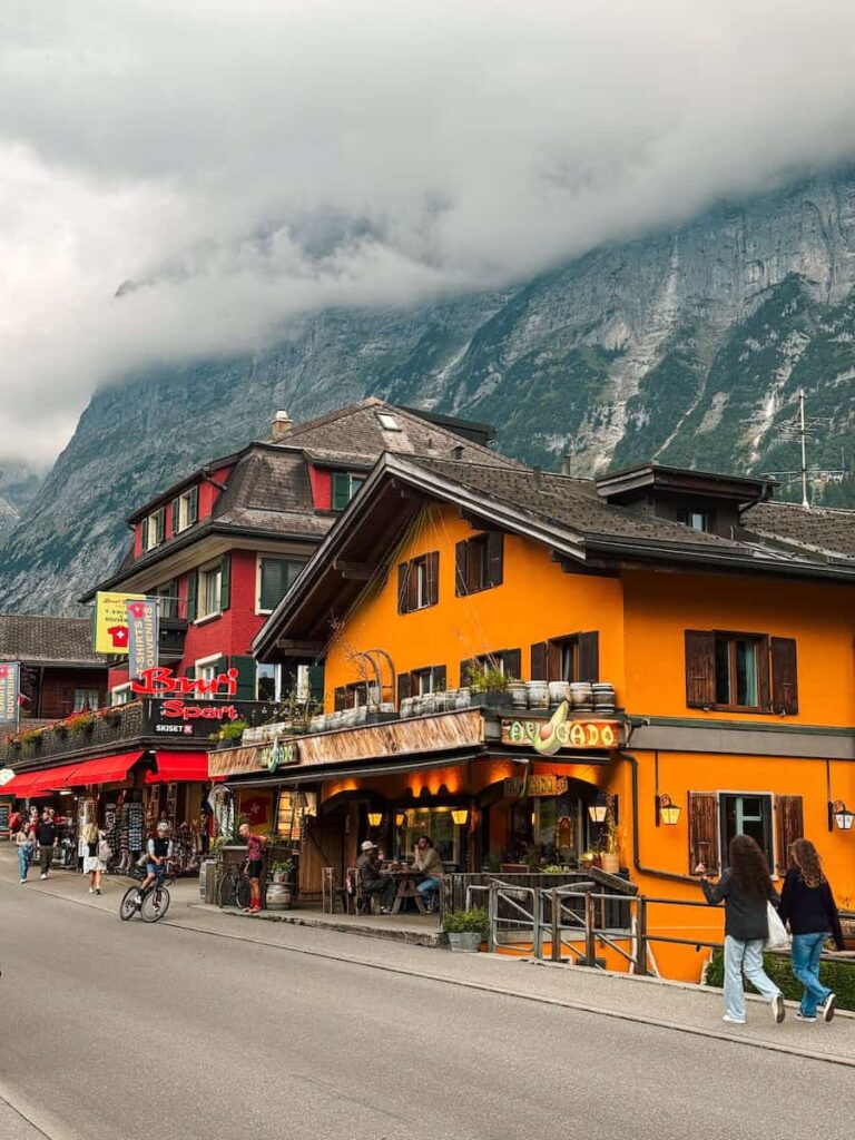 Colorful shops and restaurants along a lively street in Grindelwald with misty mountains rising dramatically behind the village.