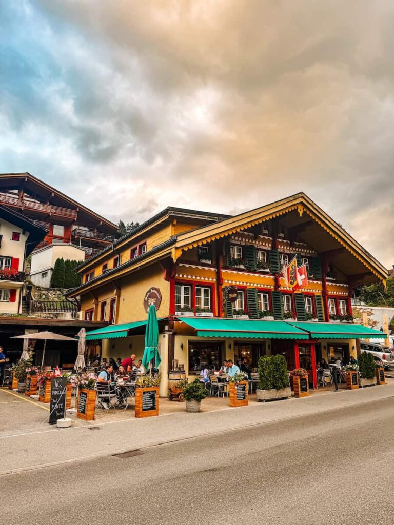 Vibrant Swiss restaurant in the village of Grindelwald with outdoor seating and alpine style architecture under a dramatic evening sky.