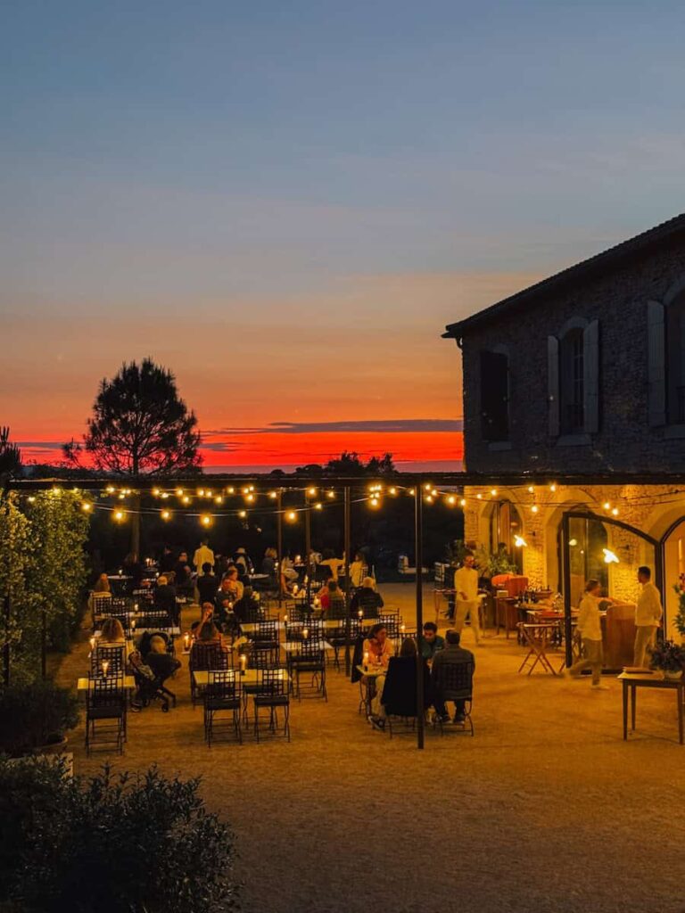 An outdoor dinner setting at sunset with string lights, stone buildings, and guests dining under the evening sky at Capelongue hotel in Provence. 