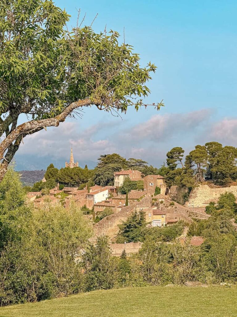 Bonnieux, a hilltop village of stone houses and a church tower surrounded by trees under a bright blue sky. As seen from Capelongue hotel's la bergerie restaurant. 