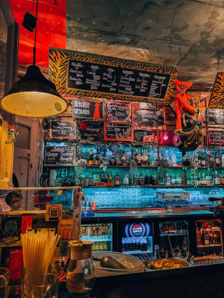 Bar counter inside Szimpla Kert featuring handwritten chalkboard menus, shelves of bottles, quirky decorations, and vibrant ambient lighting that reflects the eclectic ruin bar atmosphere.