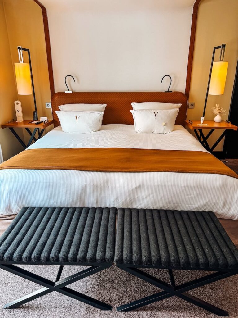 Centered view of the hotel bed at Five Seas Hotel Cannes with leather headboard matching lamps and bench at the foot of the bed