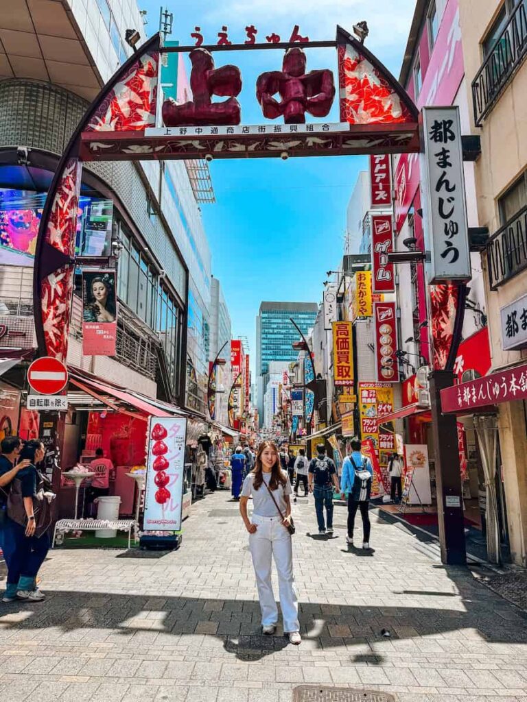 Woman standing under the Ameyoko shopping street arch in Ueno Tokyo with colorful signs and busy pedestrian street lined with shops and food stalls