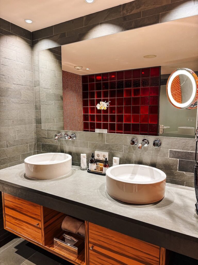 Double sink bathroom at Hotel Krallerhof with stone countertop wood cabinetry and red mosaic tile accents