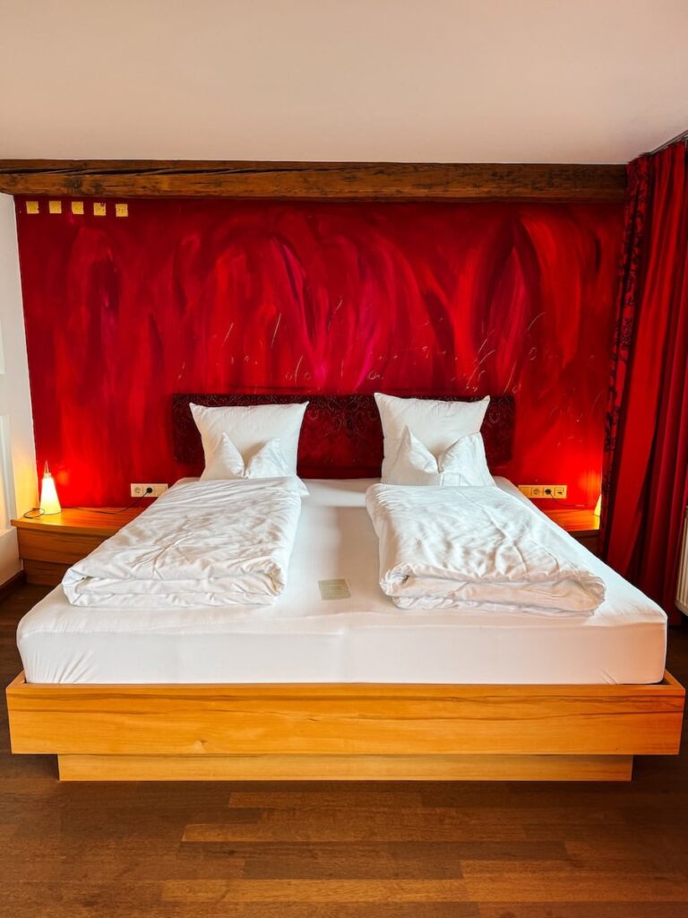 Double bed hotel room at Hotel Krallerhof with wooden bed frame white linens and bold red accent wall