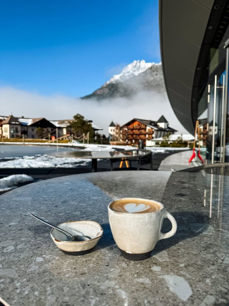 Cappuccino on an outdoor terrace at Hotel Krallerhof with snowy alpine village and mountains in the background