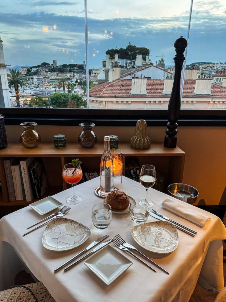 Elegant dinner table at Le Roof restaurant with city views over Cannes rooftops and harbor at sunset