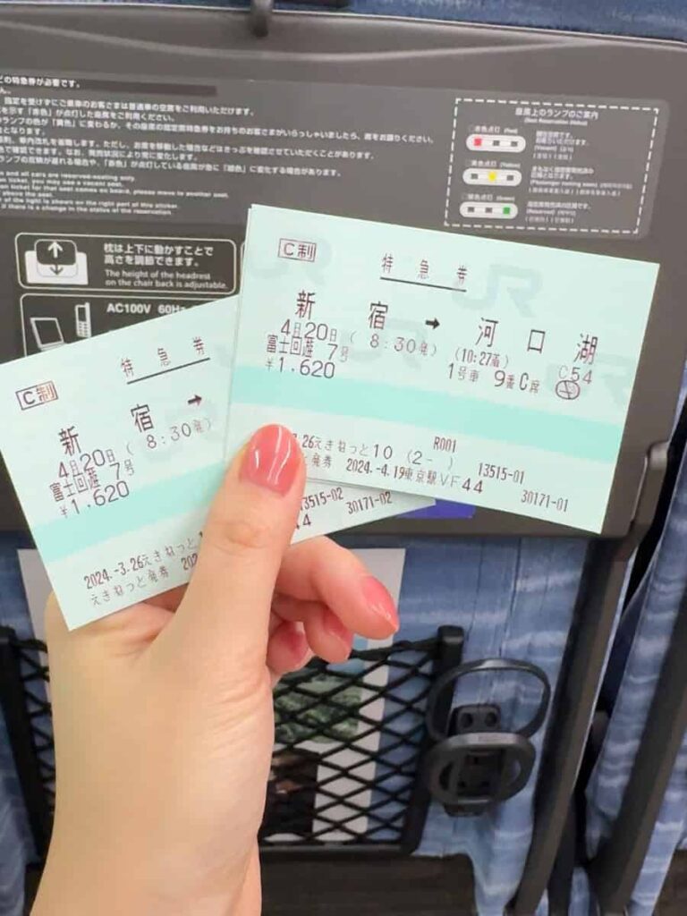 Close up of Fuji Excursion train tickets from Shinjuku to Kawaguchiko held in hand on a Japanese train seat