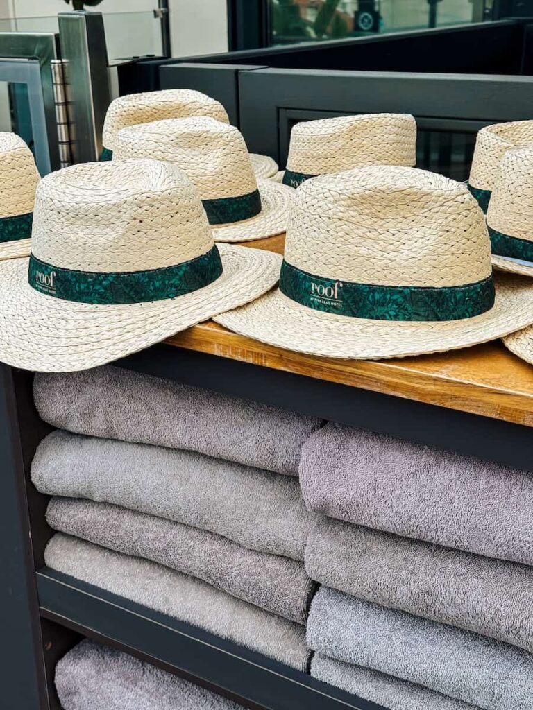 Pool amenities at Five Seas Hotel Cannes featuring rolled gray towels and straw hats branded Le Roof